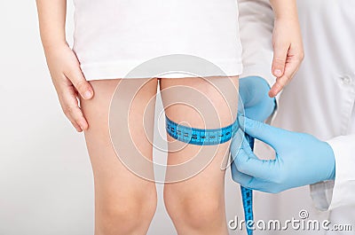 The doctor measures the thickness of the legs of a girl 4 years old with a measuring tape on a white background. The Stock Photo