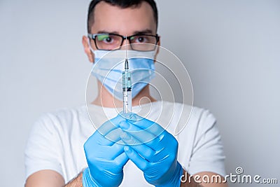 A doctor in a medical mask and gloves holds a syringe with a coronavirus vaccine and a vaccine chip inside. Conspiracy theory. Stock Photo