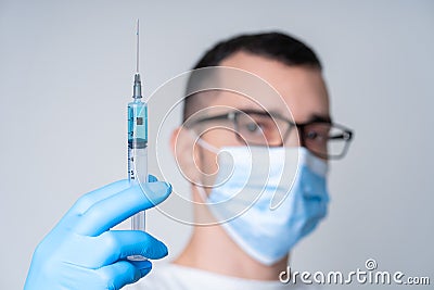A doctor in a medical mask and gloves holds a syringe with a coronavirus vaccine and a vaccine chip inside. Conspiracy theory. Stock Photo
