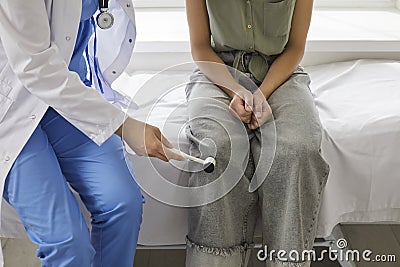 Doctor neurologist examining female patient knocking on knee with hammer in clinic closeup. Stock Photo