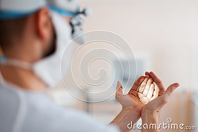 Doctor neurosurgeon in a medical mask in professional magnifying glasses shines on the hands checks binocular loupes. Stock Photo