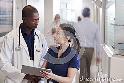 Doctor And Nurse Consulting Over Digital Tablet In Busy Hospital Corridor Stock Photo