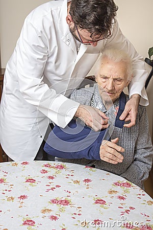 Doctor and the nurse help the old woman get up from the chair. An old woman with a hand in a sling. Stock Photo