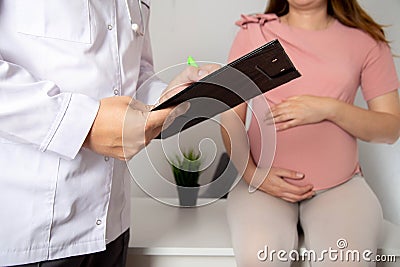 Doctor obstetrician gynecologist writes down complaints about the health of a pregnant girl in the third trimester. Polyhydramnios Stock Photo