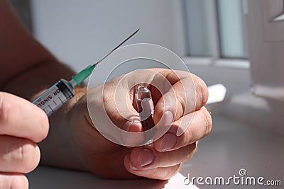 A doctor opened ampoule and hold it in one hand and a syringe in another. Stock Photo