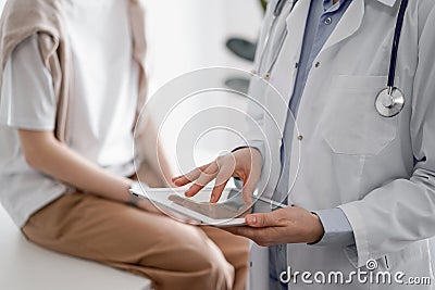 Doctor and patient in clinic. Friendly physician using tablet computer near a young woman. Medicine concept Stock Photo