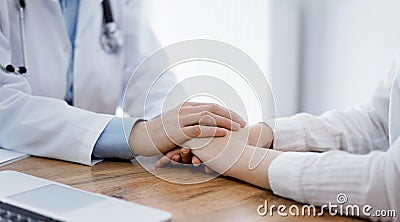 Doctor and patient sitting at the wooden table in clinic. Female physician& x27;s hands reassuring woman. Medicine Stock Photo