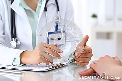 Doctor and patient talking while sitting at the desk in hospital office, closeup of human hands. Medicine and health Stock Photo