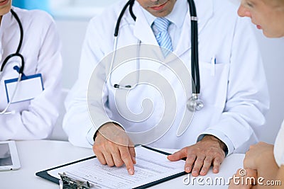 Doctor and patient talking while sitting at the desk in office. Physician pointing into medical history form. Medicin Stock Photo