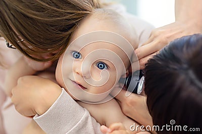 Doctor pediatrist examining childs ear with otoscope. Mom holding baby with hands. Medicine, healthcare ,pediatry and people. Stock Photo