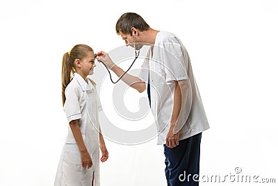 The doctor put the head of the phonendoscope to the forehead of the girl in a medical gown Stock Photo