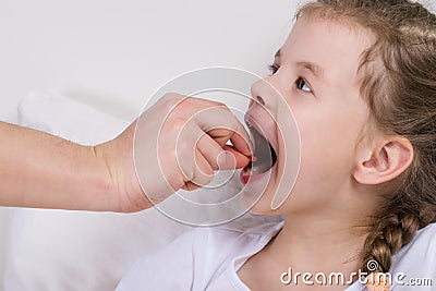 The doctor puts the pill in the little girl`s mouth, which opened Stock Photo