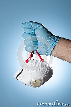 The doctor`s hand in a blue glove clutches a medical respirator, as a symbol of victory over the virus and the epidemic Stock Photo