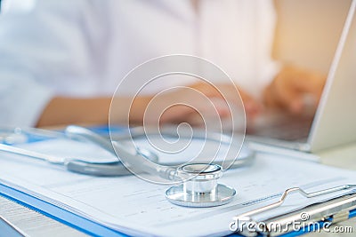 Doctor`s writing and working on laptop computer, writing prescription clipboard with record information paper folders on desk in Stock Photo