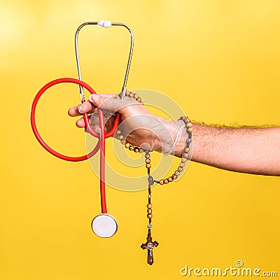 Doctor shows a religious rosary next to his stethoscope encouraging faith in the miraculous cure of science Stock Photo