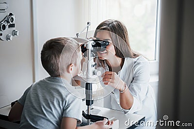 Doctor is smiling. Little boy having test for his eyes with special optical apparatus by female doctor Stock Photo