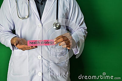 A doctor standing, Hold the Health Strategy paper text on Green background. Medical and healthcare concept Stock Photo