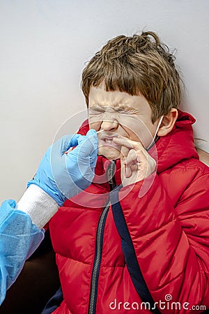 Doctor tacking a coronavirus test to an elementary age boy's nose with a medical swab. Respiratory virus testing procedure Stock Photo