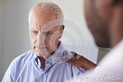 Doctor Talking To Unhappy Male Patient In Exam Room Stock Photo