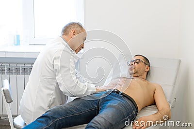 Doctor therapist probes the stomach of a male patient who is lying on a couch. Professional medical advice Stock Photo