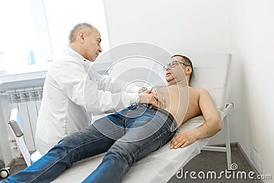 Doctor therapist probes the stomach of a male patient who is lying on a couch. Professional medical advice Stock Photo