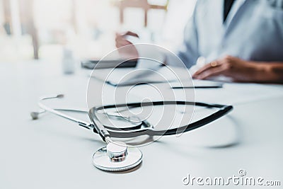 Doctor typing information on Laptop in Hospital office focus on Stethoscope Stock Photo