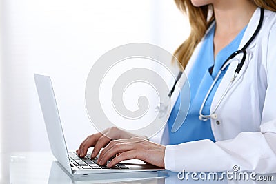 Doctor typing on laptop computer while sitting at the glass desk in hospital office. Physician at work. Medicine and Stock Photo