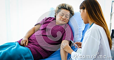 The doctor is using the syringe for the sick old woman lying on the bed Stock Photo