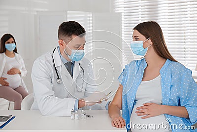 Doctor vaccinating pregnant woman against Covid-19 in clinic Stock Photo