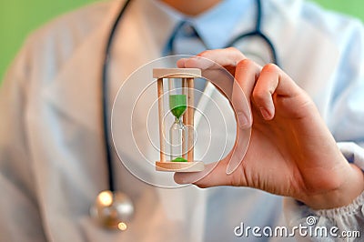 A doctor in white medical gloves holds an hourglass - a symbol of time to heal and cure. Close up Stock Photo