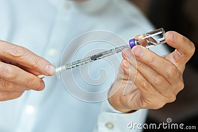 Doctor in a white surgical gown and blue mask holds in hands a medical syringe and bottle with insulin for diabetes. Sugar Stock Photo