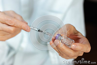 Doctor in a white surgical gown and blue mask holds in hands a medical syringe and bottle with insulin for diabetes. Sugar Stock Photo