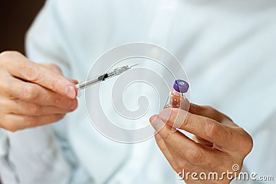 Doctor in a white surgical gown and blue mask holds in hands a medical syringe and bottle with insulin for diabetes. Sugar Stock Photo