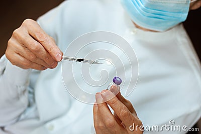 Doctor in a white surgical gown and blue mask holds in hands a medical syringe and bottle with insulin for diabetes. Sugar Stock Photo