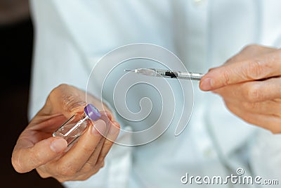 Doctor in a white surgical gown and blue mask holds in hands a medical syringe and bottle with insulin for diabetes. Sugar Stock Photo
