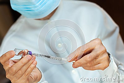 Doctor in a white surgical gown and blue mask holds in hands a medical syringe and bottle with insulin for diabetes. Sugar Stock Photo