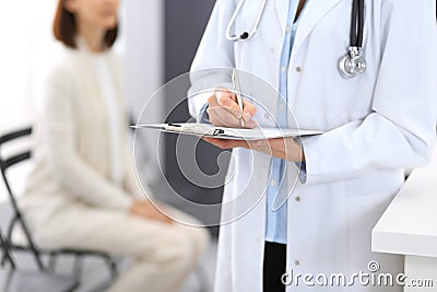 Doctor woman filling up medical form while standing near reception desk at clinic or emergency hospital.Unknown Stock Photo