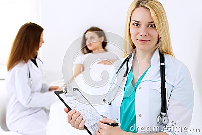 Doctor woman or nurse in a hospital office with her colleague and patient in the background. Healthcare and medicine Stock Photo