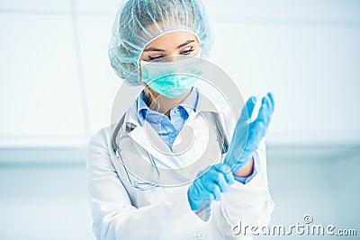 Doctor woman surgeon specialist in sterile clothing putting on surgical gloves Stock Photo