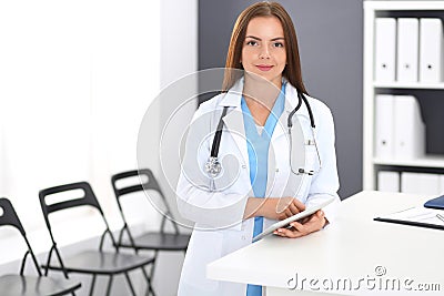 Doctor woman at work. Portrait of female physician using digital tablet while standing near reception desk at clinic o Stock Photo