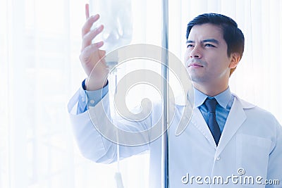 Doctor working, checking Intravenous drip, I.V. tube saline fluid bag for cure patient in hospital room. Handsome professional doc Stock Photo