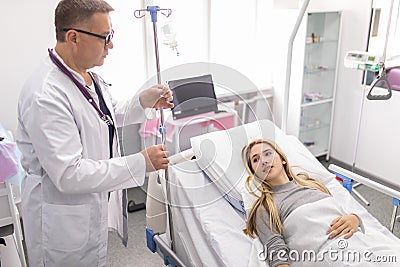 Doctor working, checking Intravenous drip, I.V. tube saline fluid bag for cure patient in hospital room. Handsome professional Stock Photo