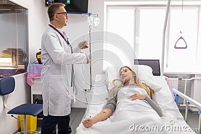 Doctor working, checking Intravenous drip, I.V. tube saline fluid bag for cure patient in hospital room. Handsome professional Stock Photo