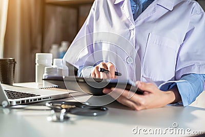 Doctor working on laptop computer, writing prescription clipboard with record information paper folders on desk. Stock Photo