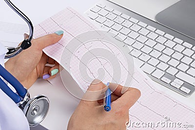 Doctor workplace. Electrocardiogram, ecg in hand of a female doctor with ekg graph paper in hospital office room with computer Stock Photo