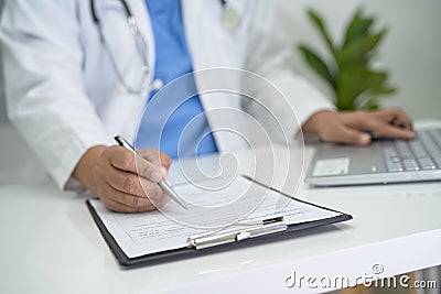 Doctor write health medical note in clipboard with laptop in hospital Stock Photo