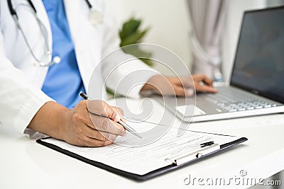 Doctor write health medical note in clipboard with laptop in hospital Stock Photo