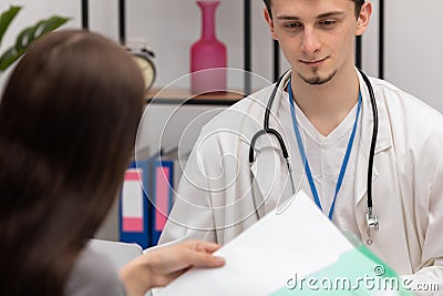 A young patient takes lab results out of her folder. Primary care physician. Doctor's office Stock Photo