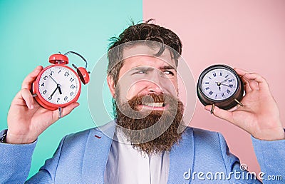 Does changing clock mess with your health. Man bearded hipster hold two different clocks. Guy unshaven puzzled face Stock Photo