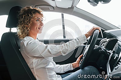 Doing test drive. Woman with curly blonde hair is in autosalon Stock Photo